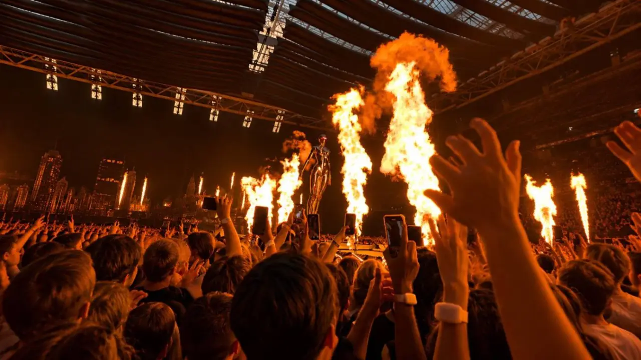 The Weeknd on stage in a stadium, flames and the crowd with hands raised